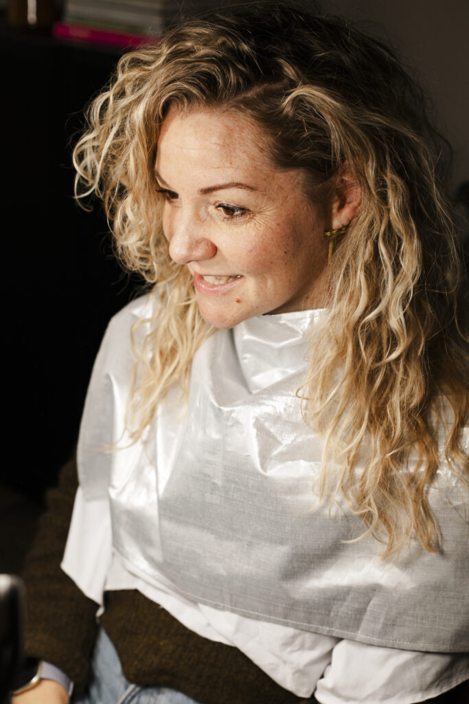 Henriette voor de spiegel tijdens een kleuranalyse met een zilverdoek om.