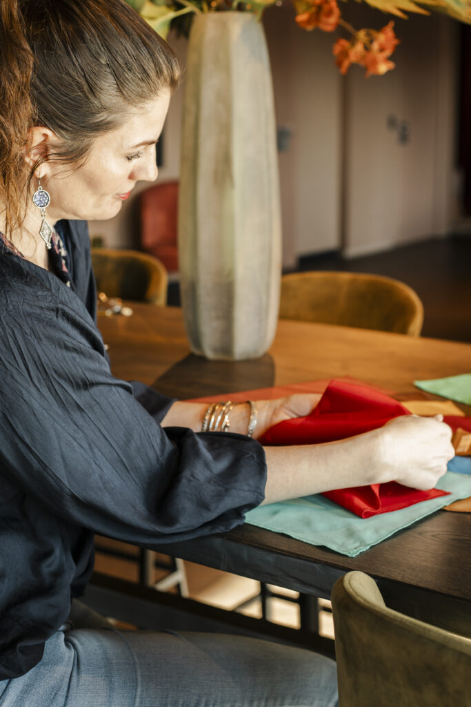 Personal branding shoot van kleurconsulent Rachel. Ze zit aan tafel en heeft kleur doeken in haar hand.